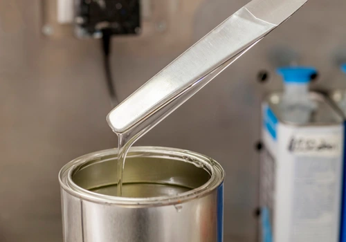 Líquido blanco cayendo en barril metálico como representación de resinas y coagentes industriales para caucho y plásticos